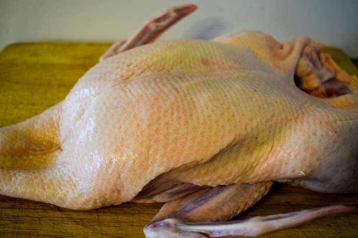 A whole raw duck on a cutting board.